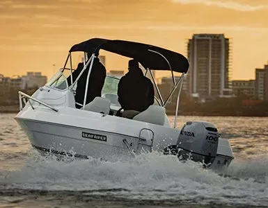 White Motorboat with Two Figures, Black Canopy, on Water with City Skyline at Sunset — HiTune Marine In Port Douglas, QLD 