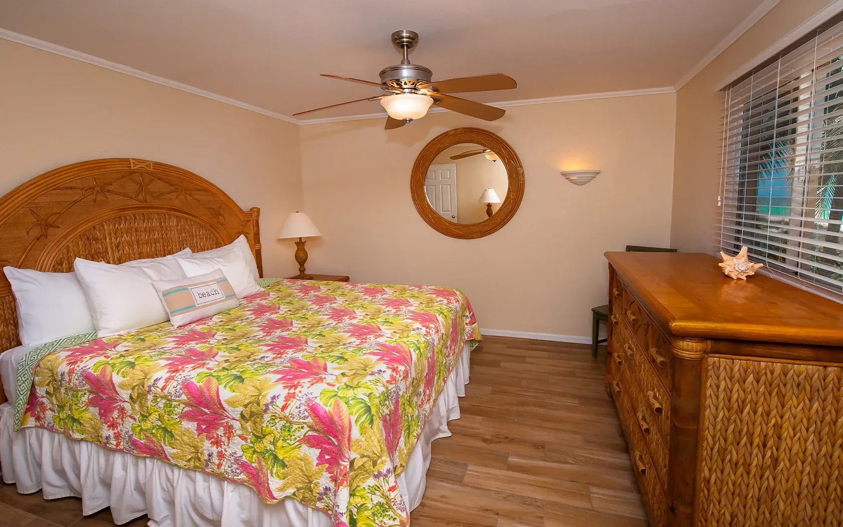 A bedroom with a king size bed , dresser , mirror and ceiling fan.