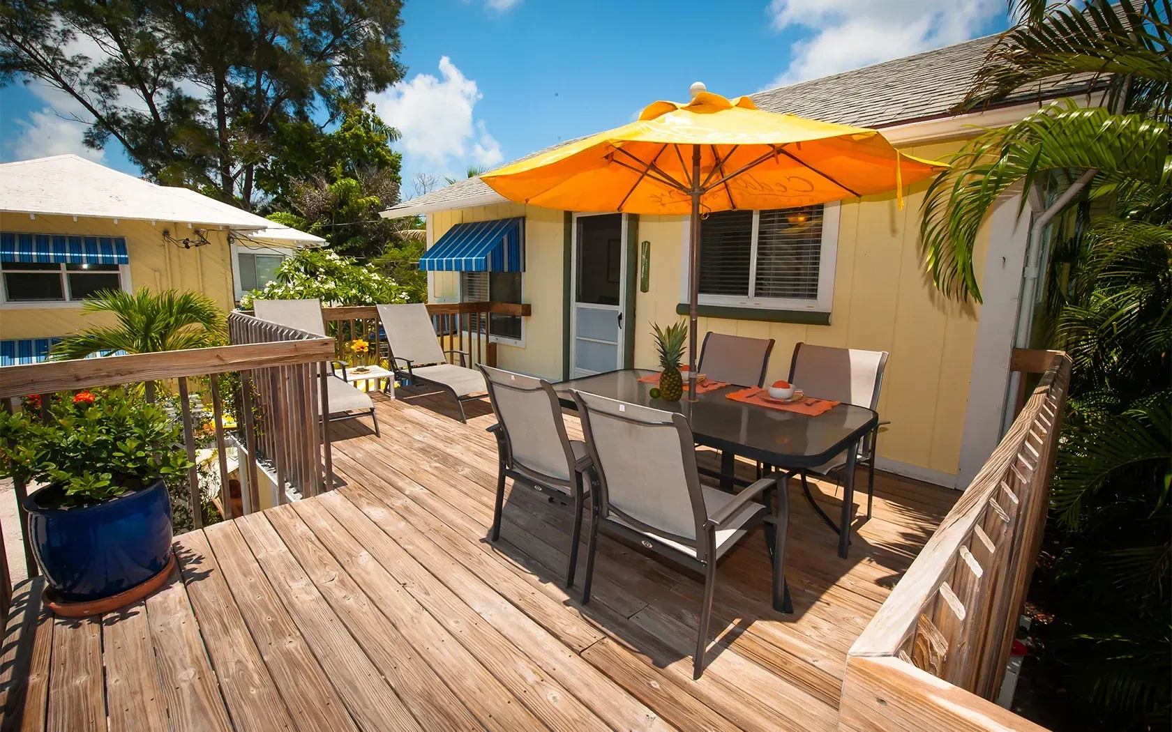 A wooden deck with a table and chairs under an orange umbrella