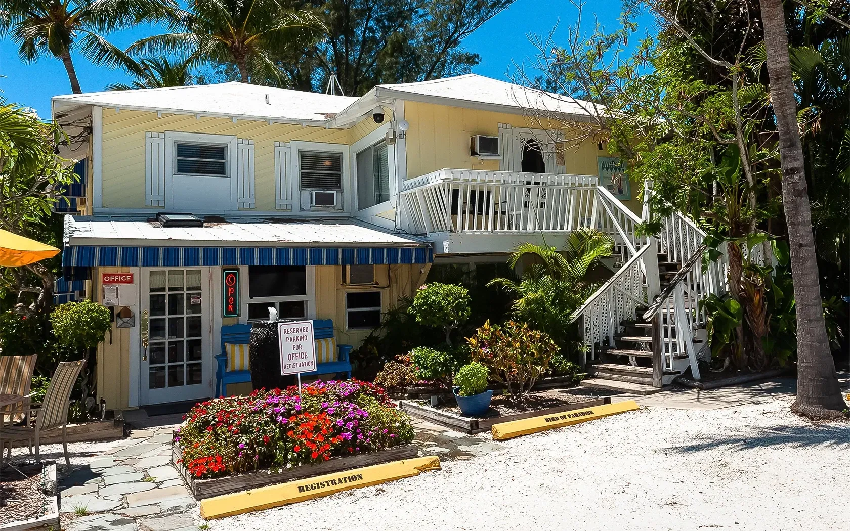 A yellow house with a blue awning and flowers in front of it