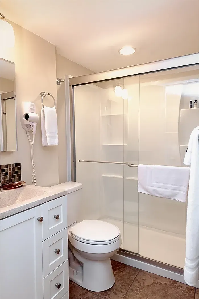 A bathroom with a toilet , sink , mirror and shower stall.