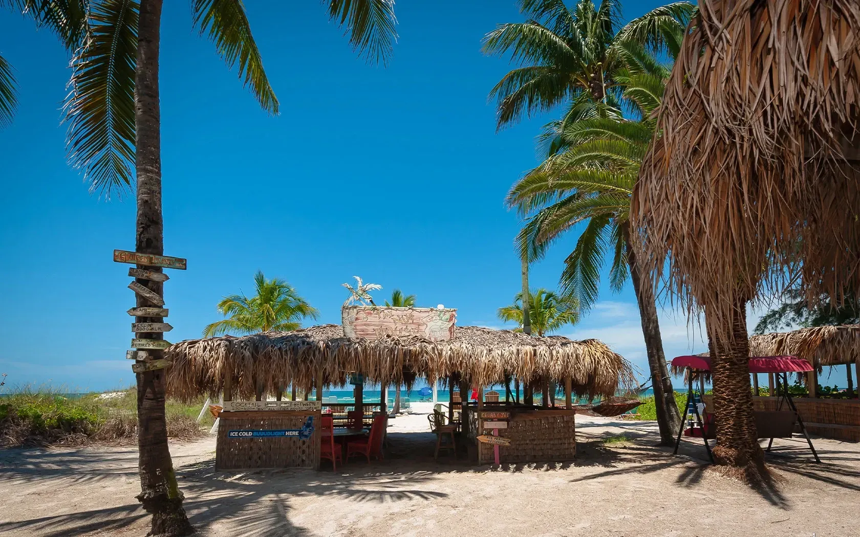 A thatched hut on a beach surrounded by palm trees.