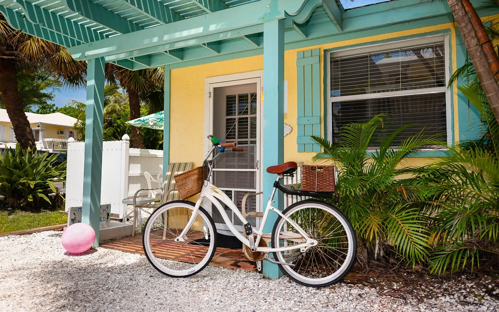 A white bicycle is parked in front of a yellow and blue house.