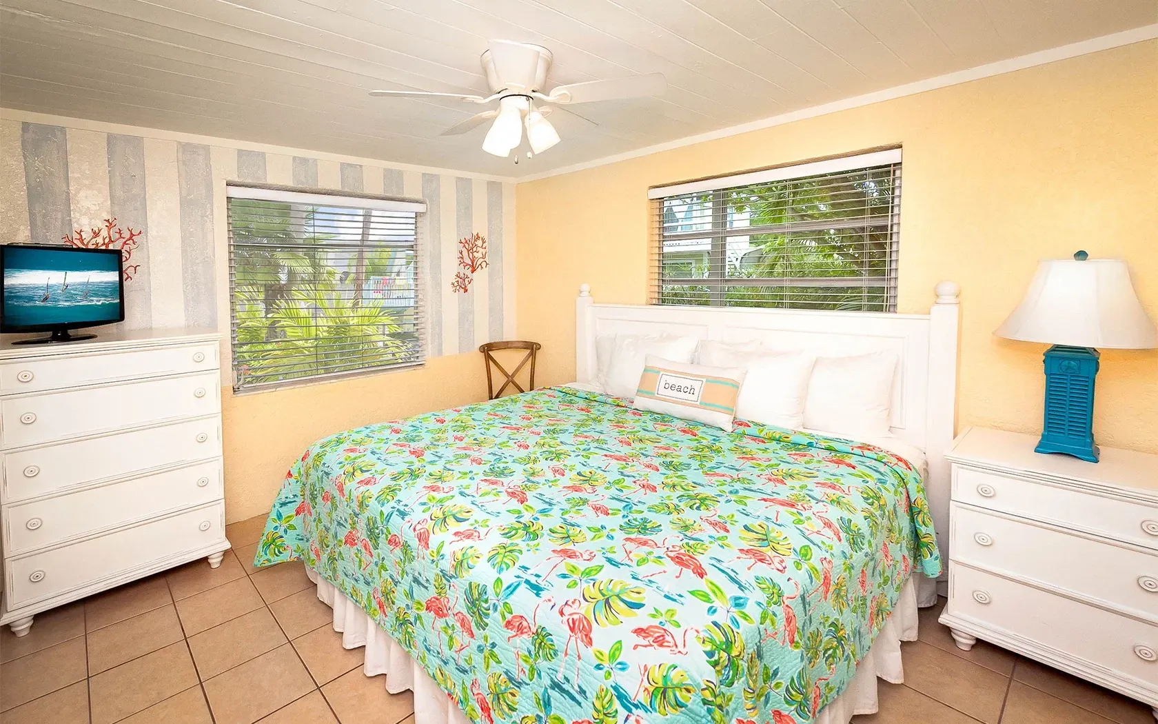 A bedroom with a king size bed , dresser , lamp and television.