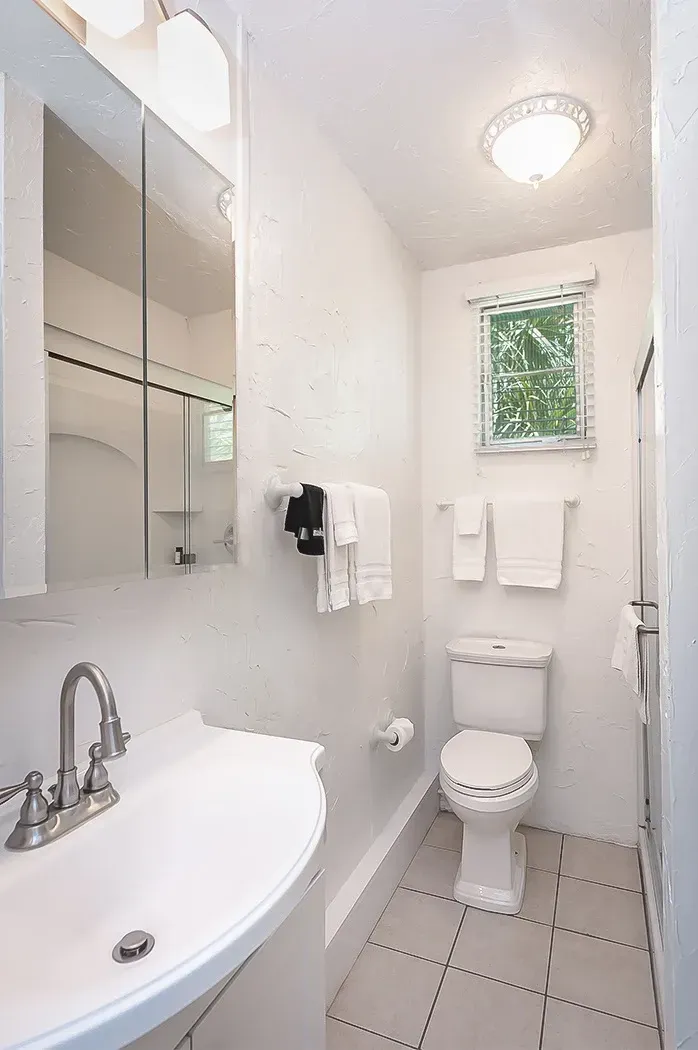 A bathroom with a toilet , sink , mirror and window