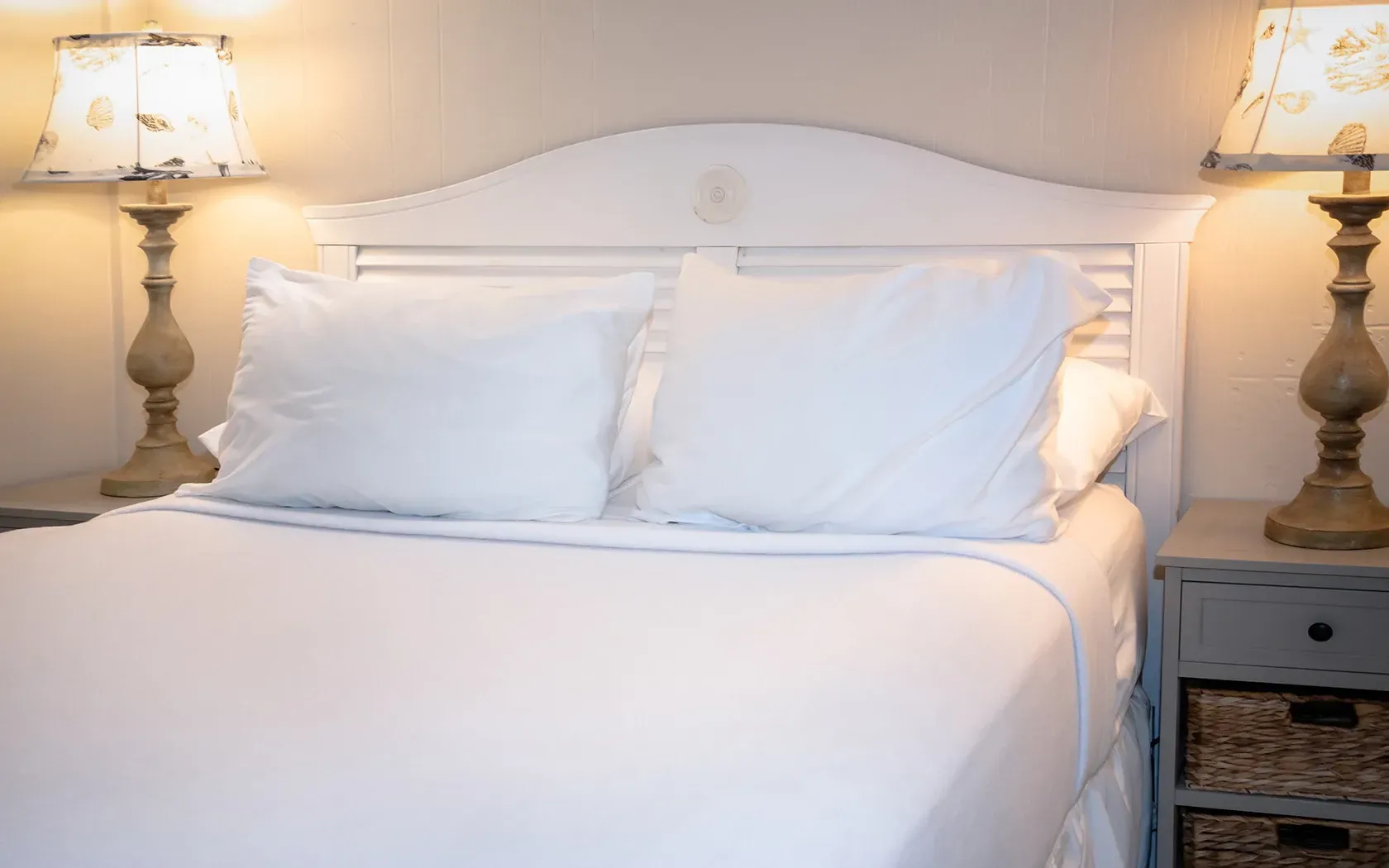 A bed with white sheets and pillows in a bedroom with two lamps.