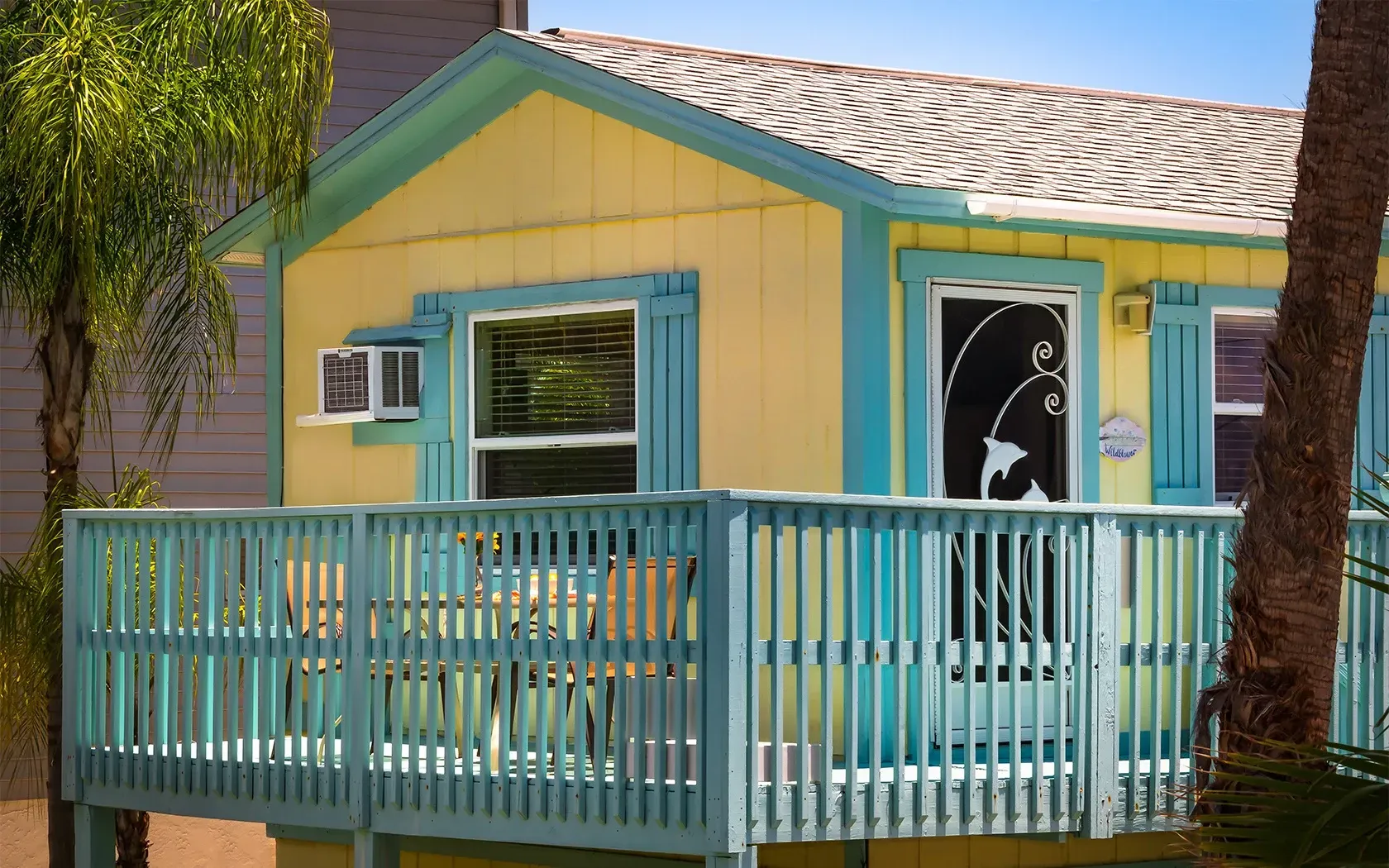 A small yellow and blue house with a blue deck