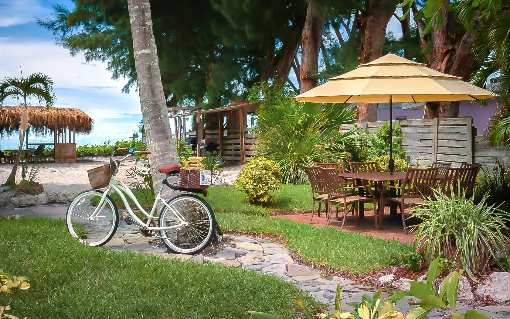 A bicycle is parked in the grass next to a table and chairs under an umbrella.