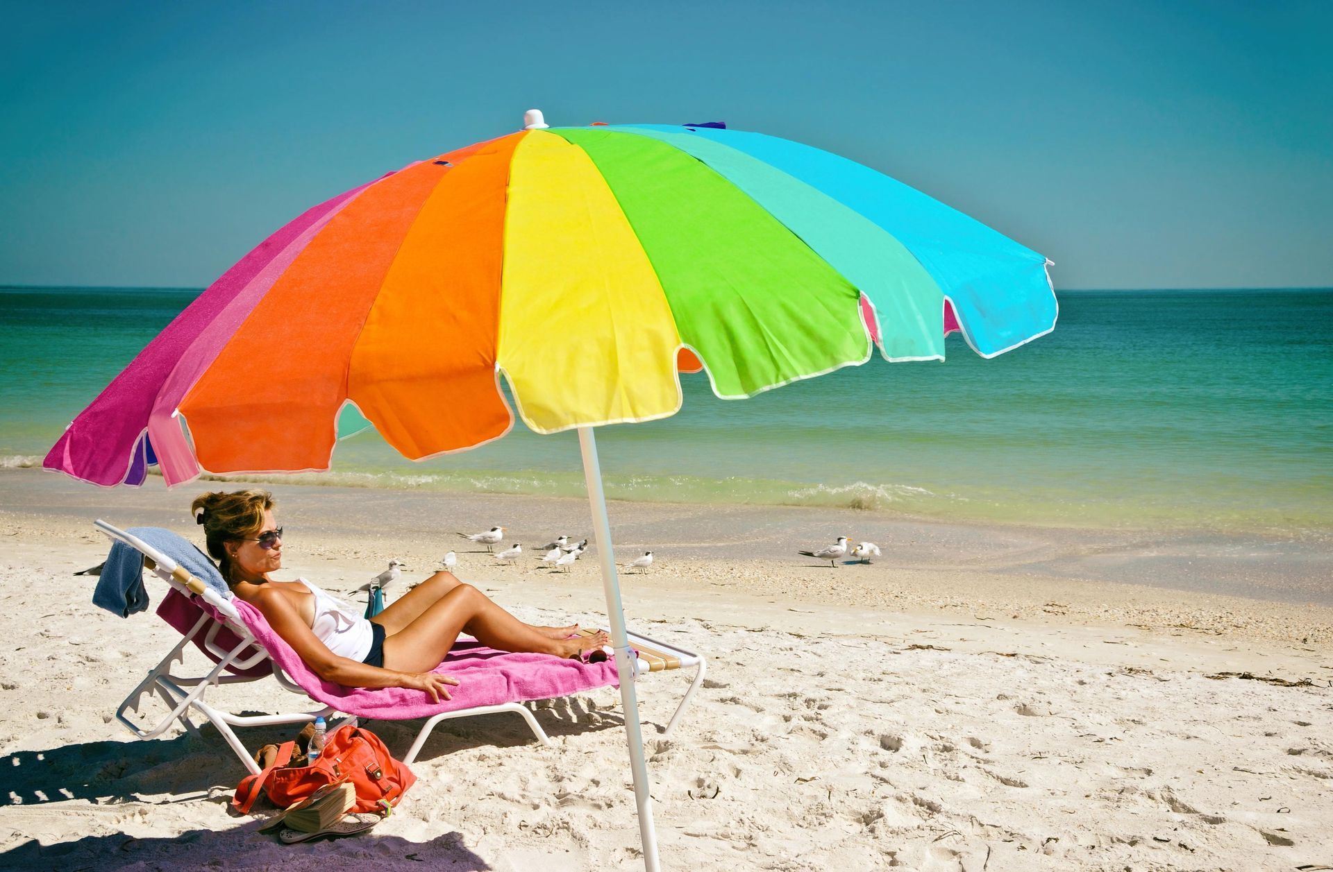 A woman is laying under a colorful umbrella on the beach