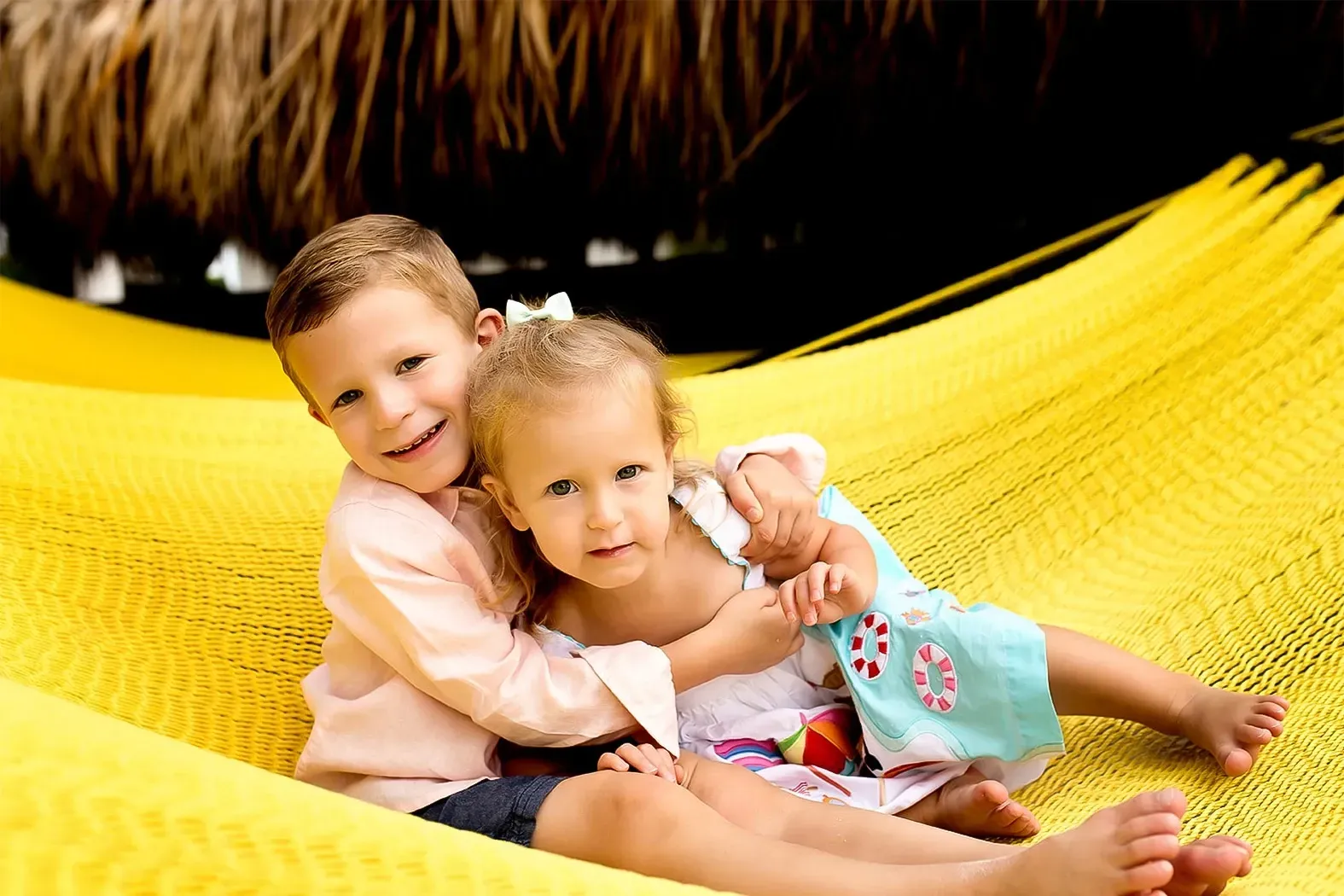 A boy and a girl are sitting in a yellow hammock.