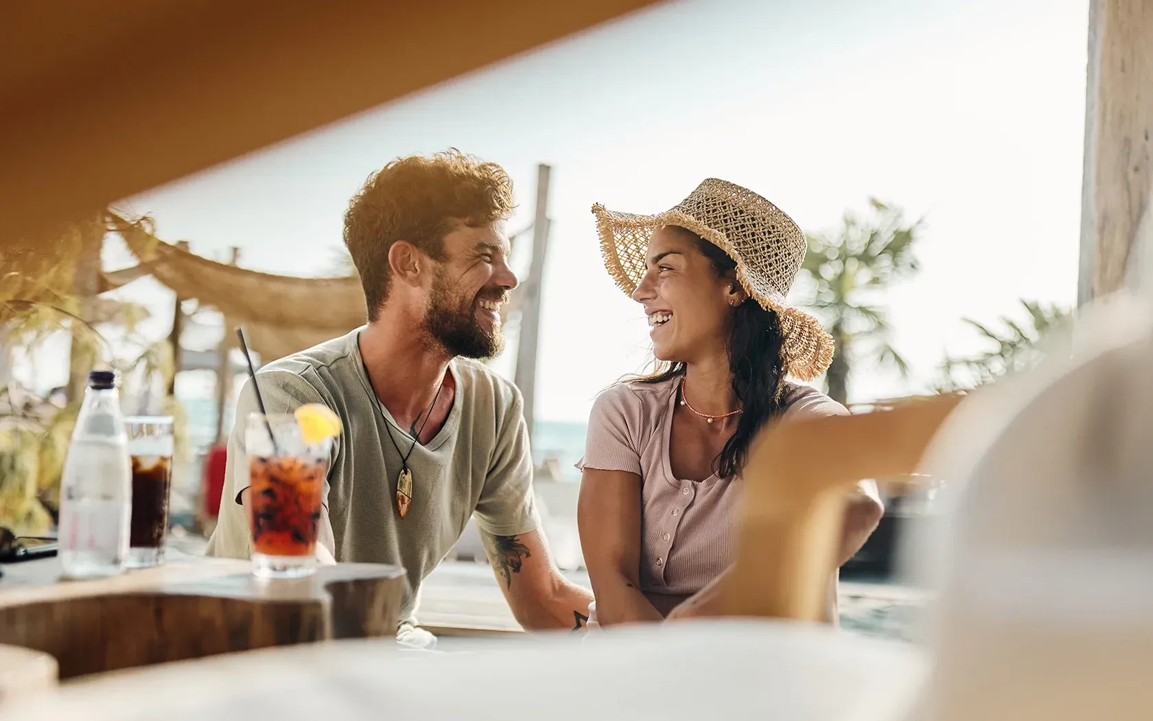 A man and a woman are sitting at a table with drinks and looking at each other.