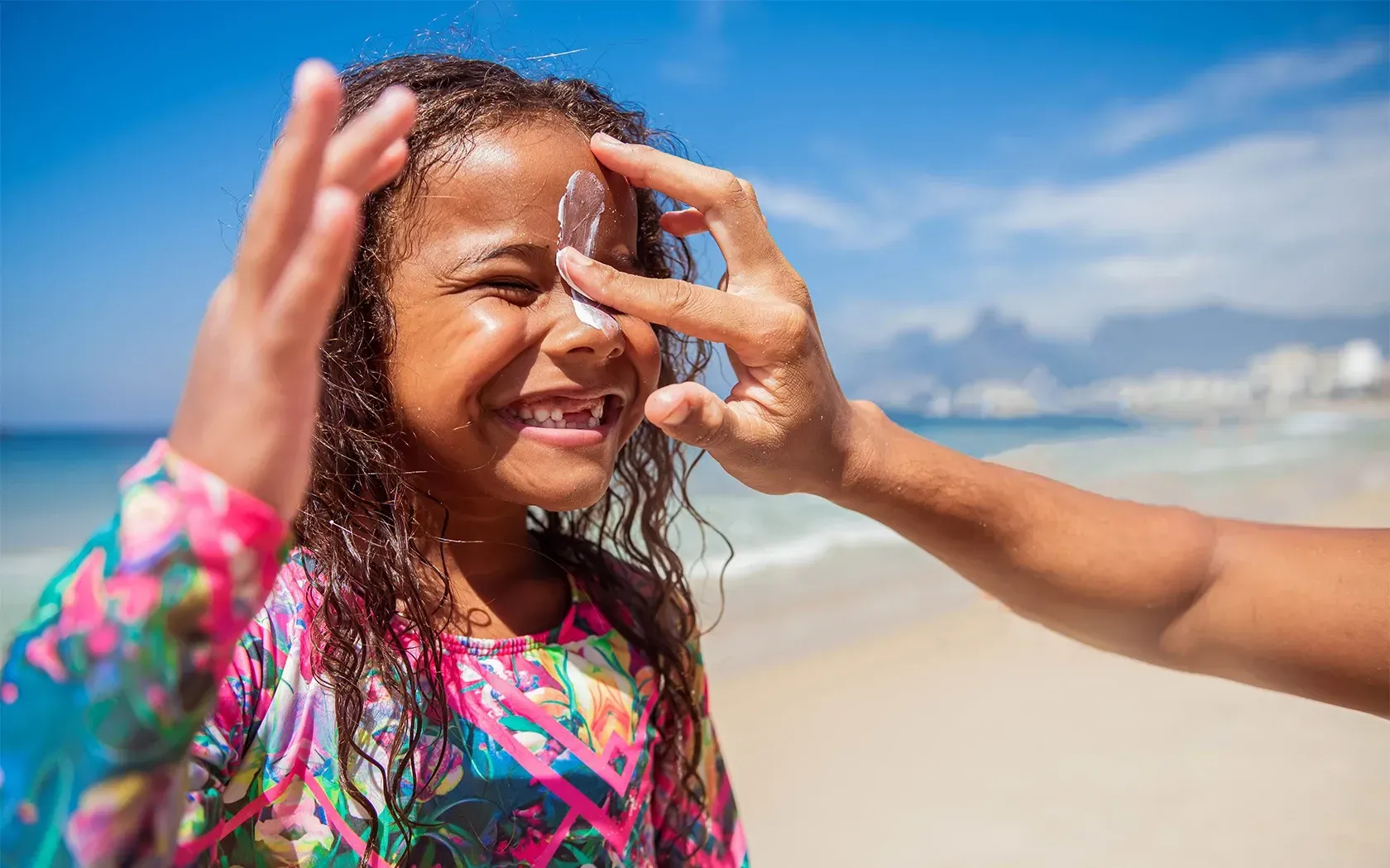 A woman is applying sunscreen to a little girl 's face on the beach.