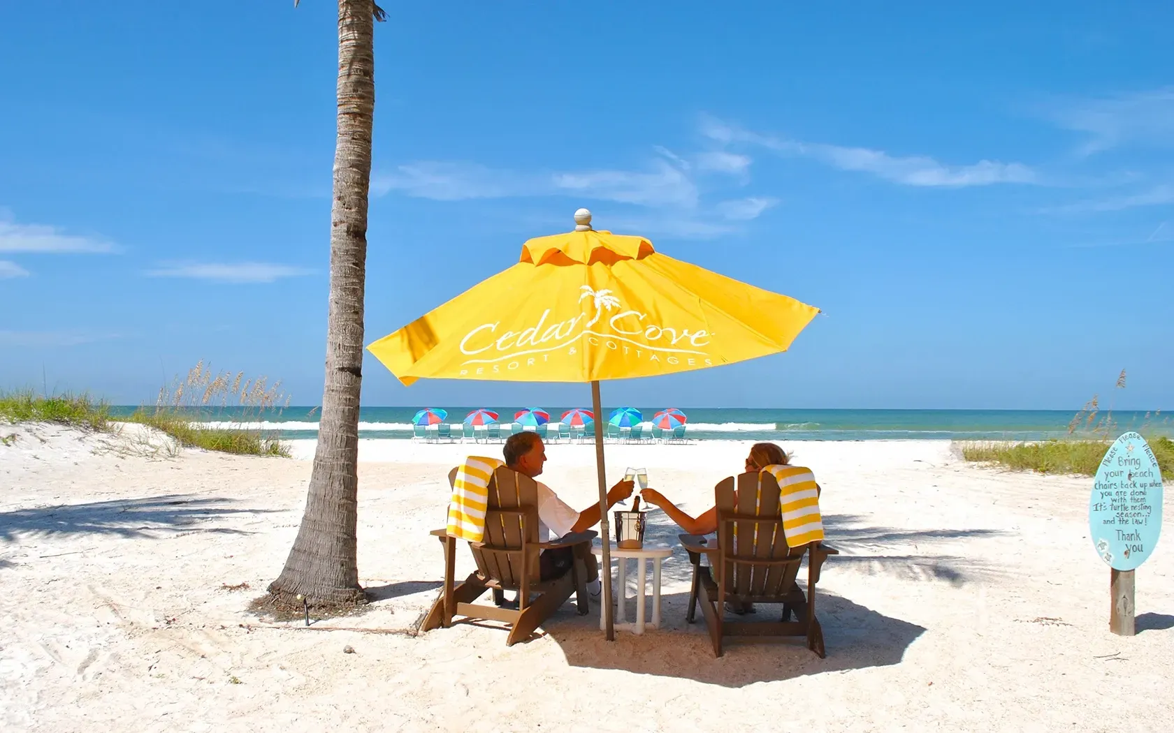 Two people are sitting under a yellow umbrella on the beach