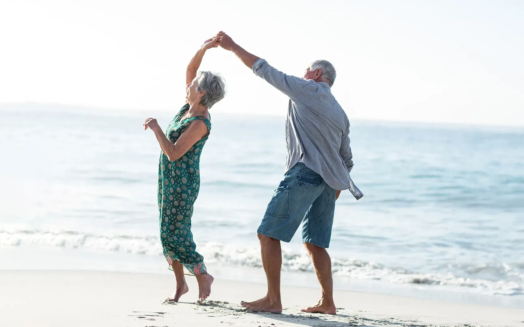 An elderly couple is dancing on the beach.