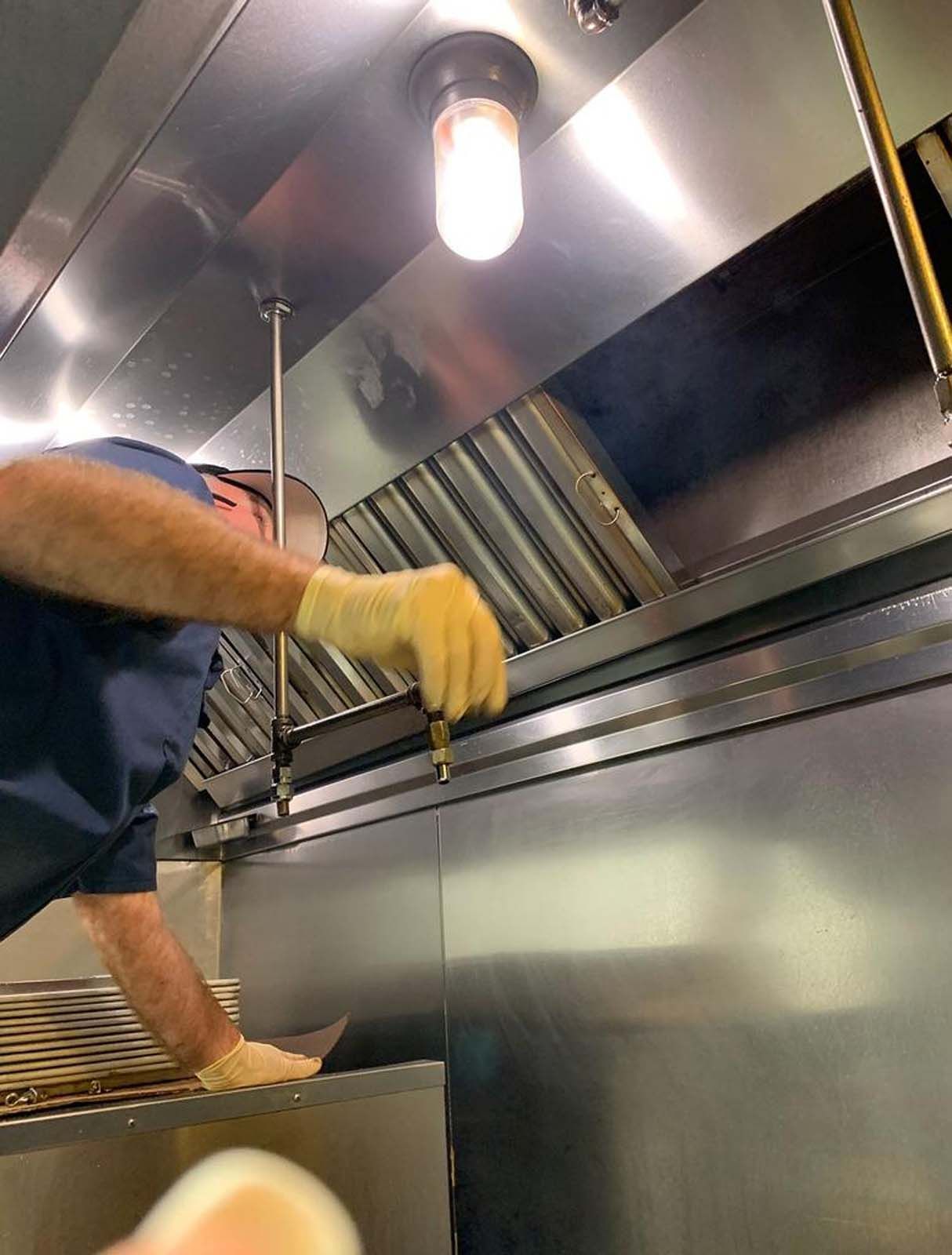 Person in gloves inspects a kitchen exhaust hood, likely for maintenance or cleaning.