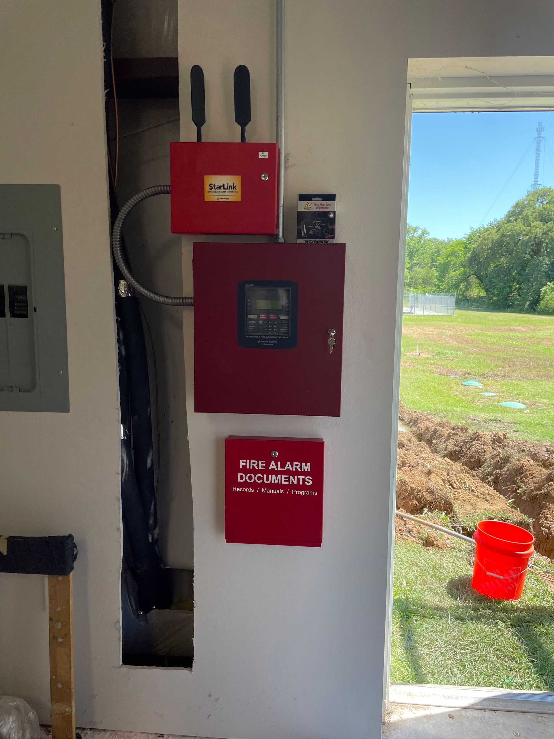 Red fire alarm system components mounted on a white wall.