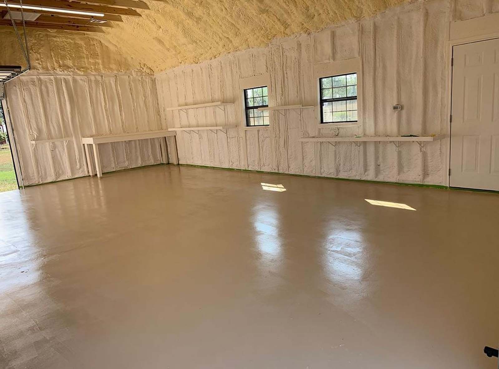 Interior of a garage with spray foam insulation, two windows, and a shiny, neutral-colored floor.