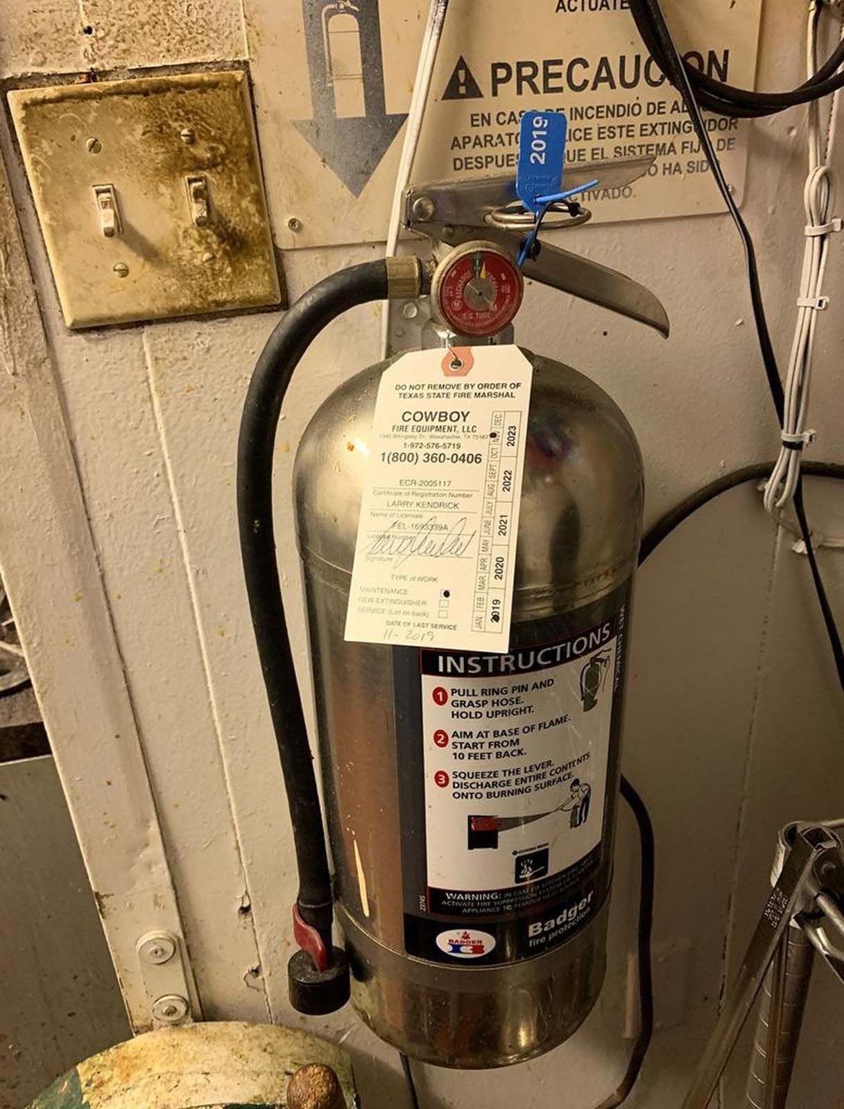 Stainless steel fire extinguisher hanging on a wall with a tag and instructions visible.