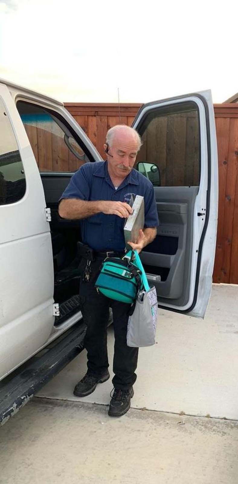 A person near a white van, opening a metal case, holding a turquoise bag.