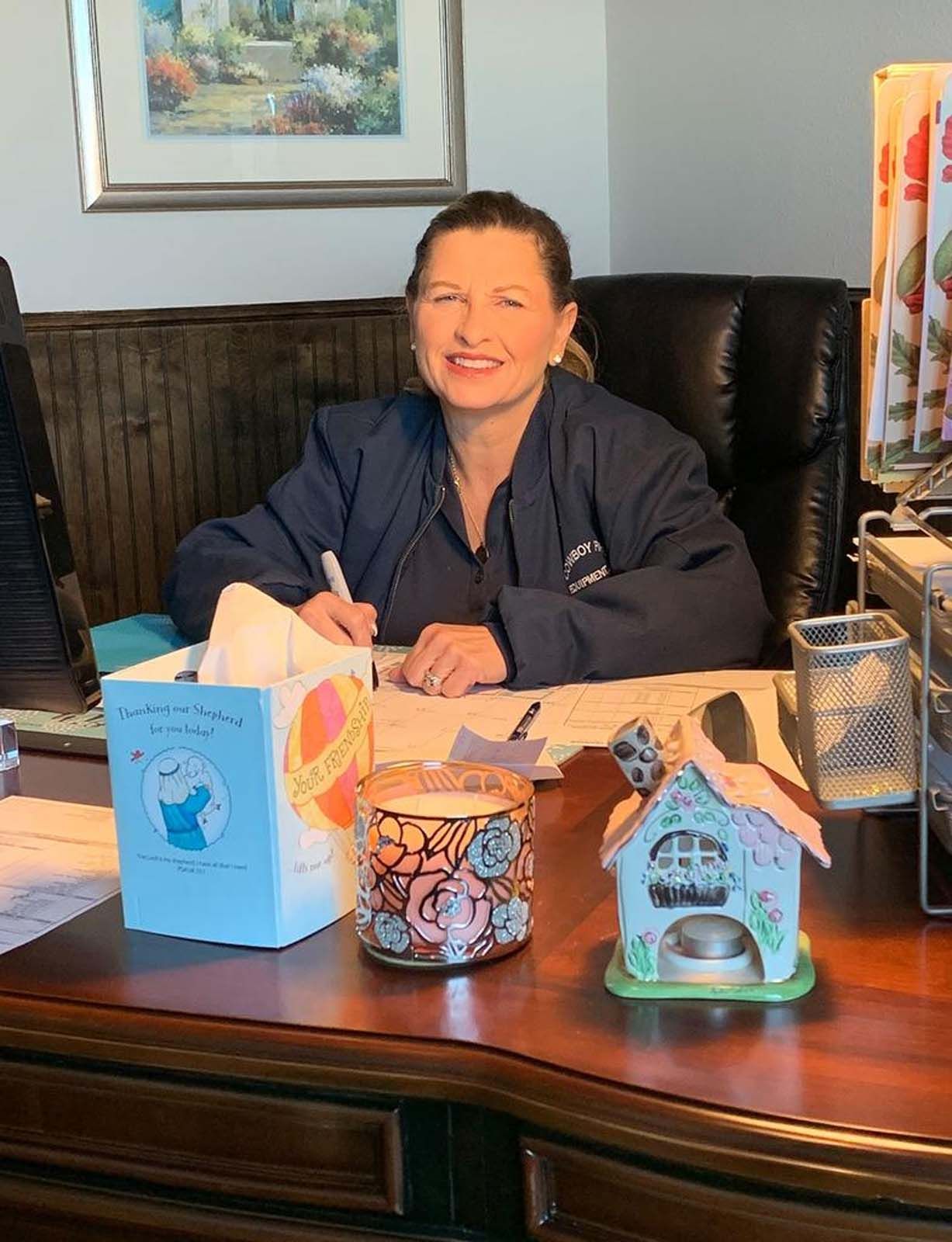 Woman at desk, writing. Desk has tissue box, candle, and house-shaped holder.