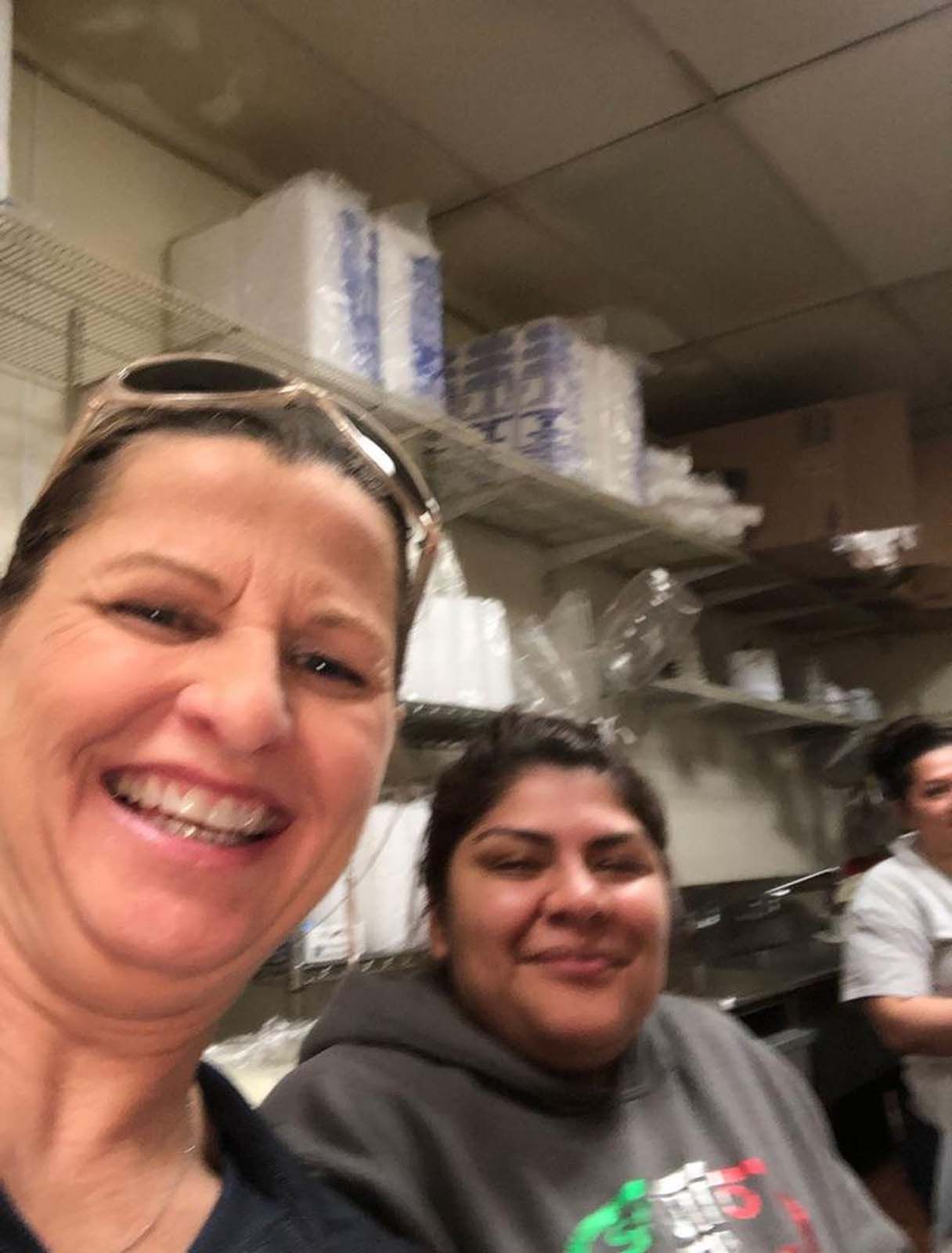 Two women smiling in a workspace with shelves of supplies.