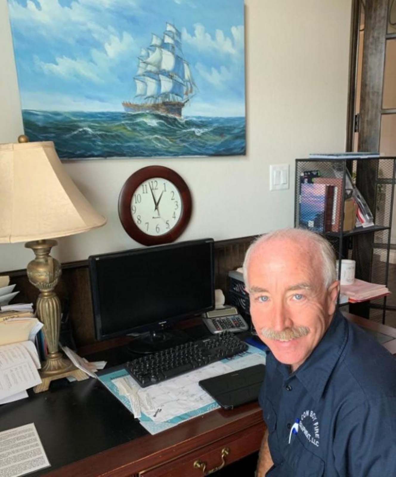 Man at desk with a computer and papers, smiling.