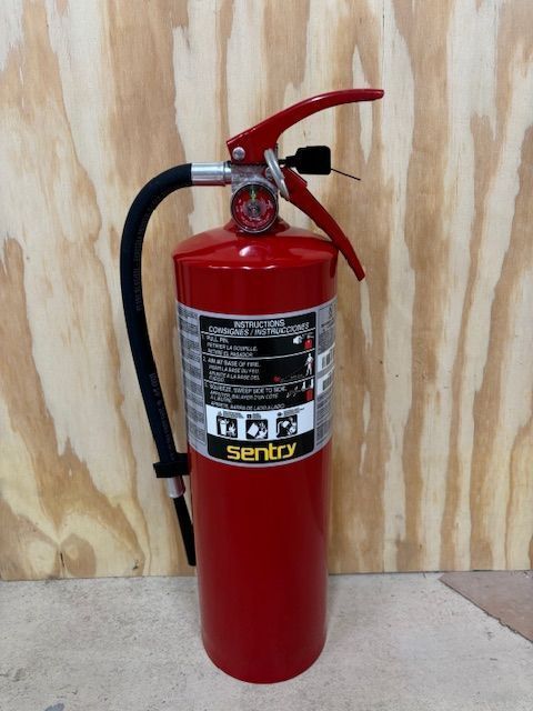 Red fire extinguisher with black hose against a wood background.
