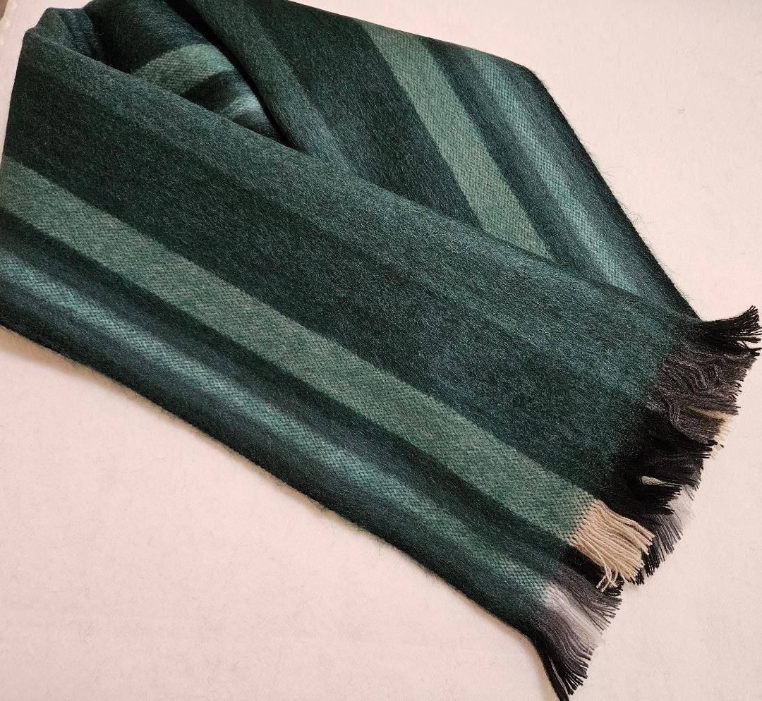 A green scarf with fringe is laying on a white surface