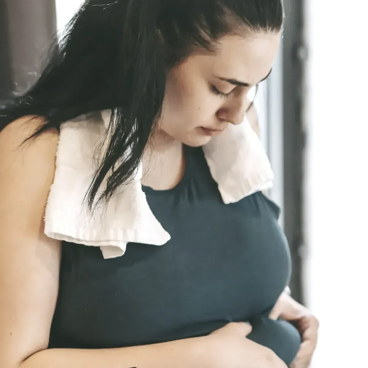 A woman with a towel around her neck is holding her belly