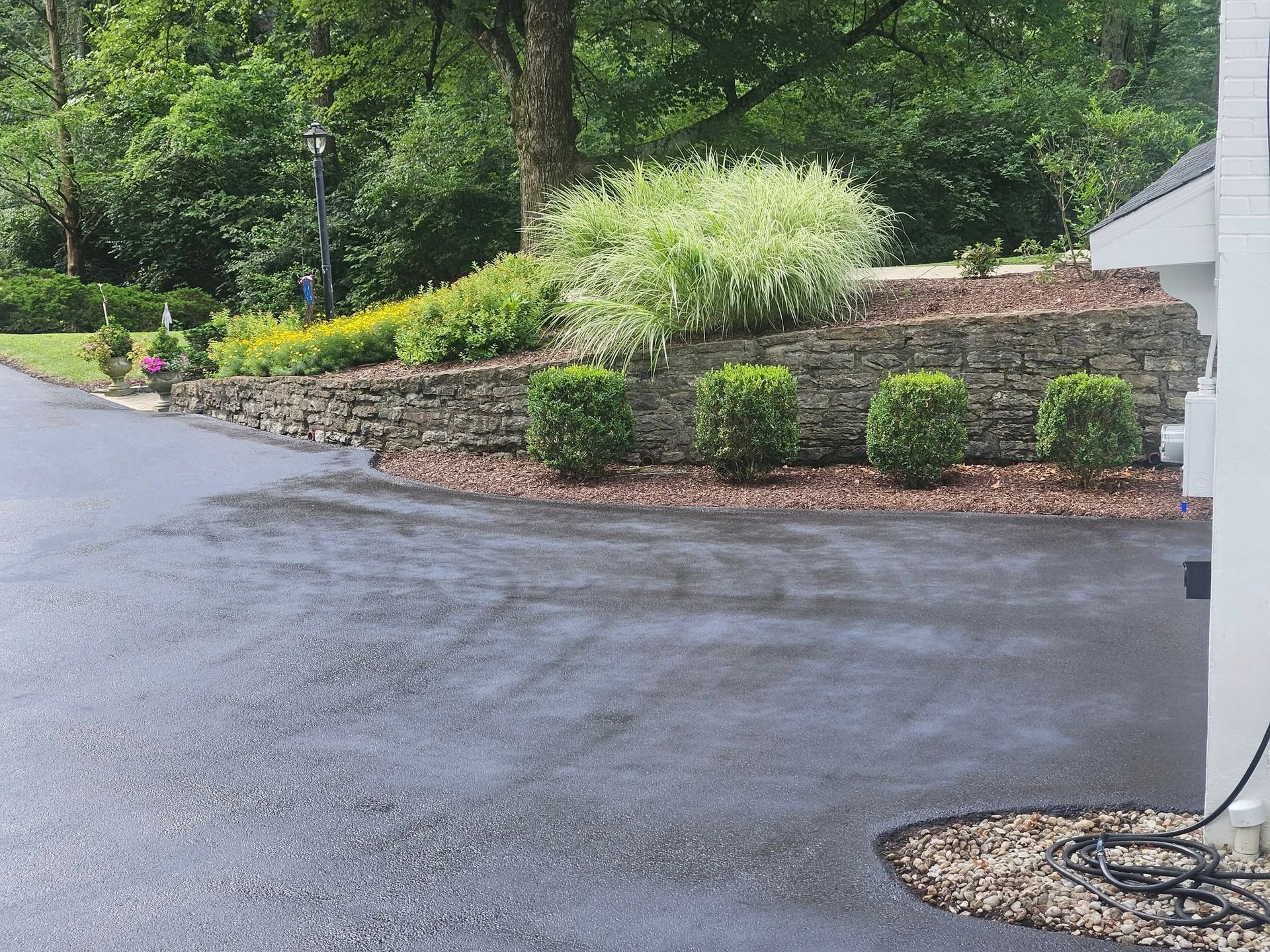 A driveway with a stone wall and bushes on the side of it