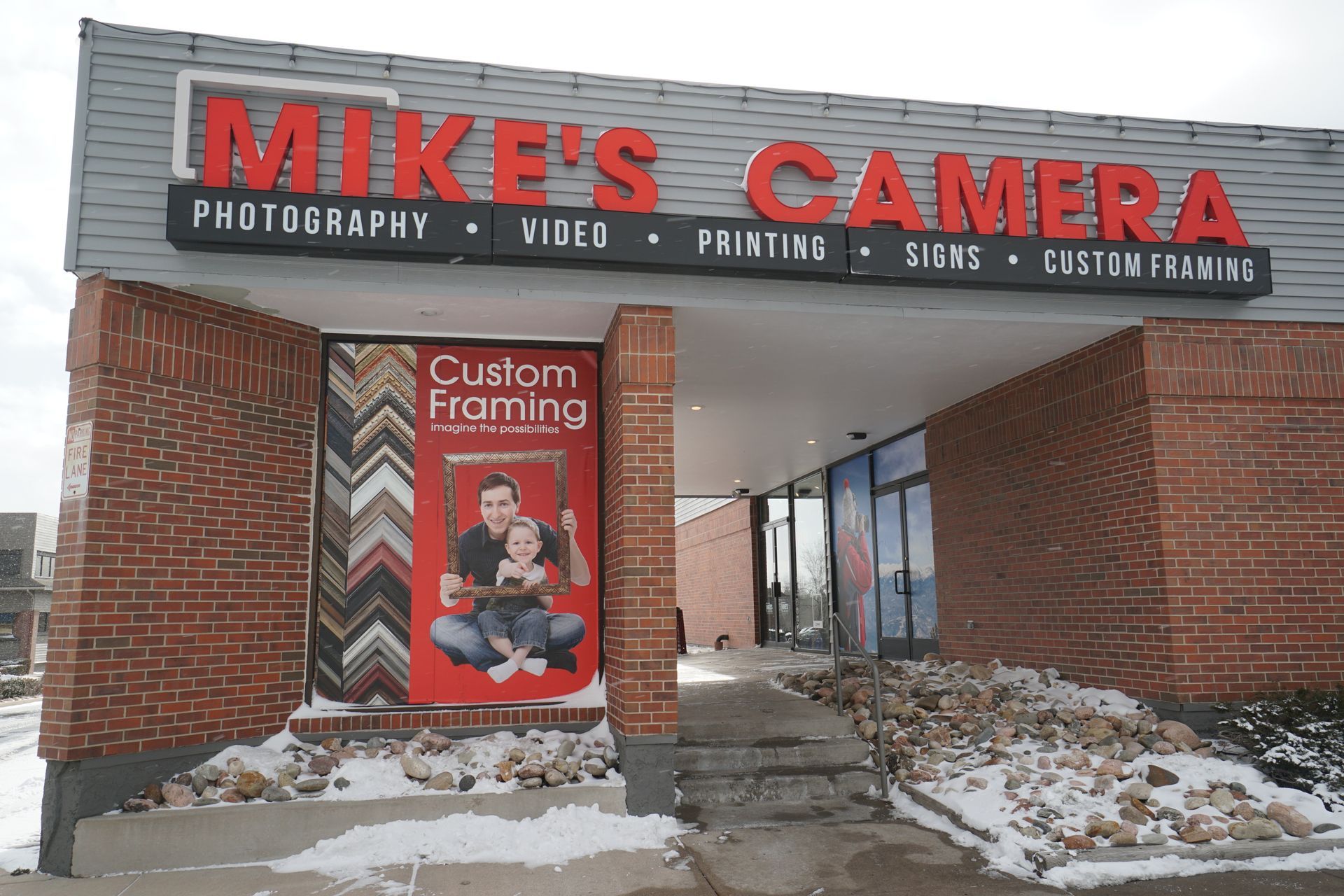 Mike's Camera store front with red sign on a gray building, brick accents, and parked car.