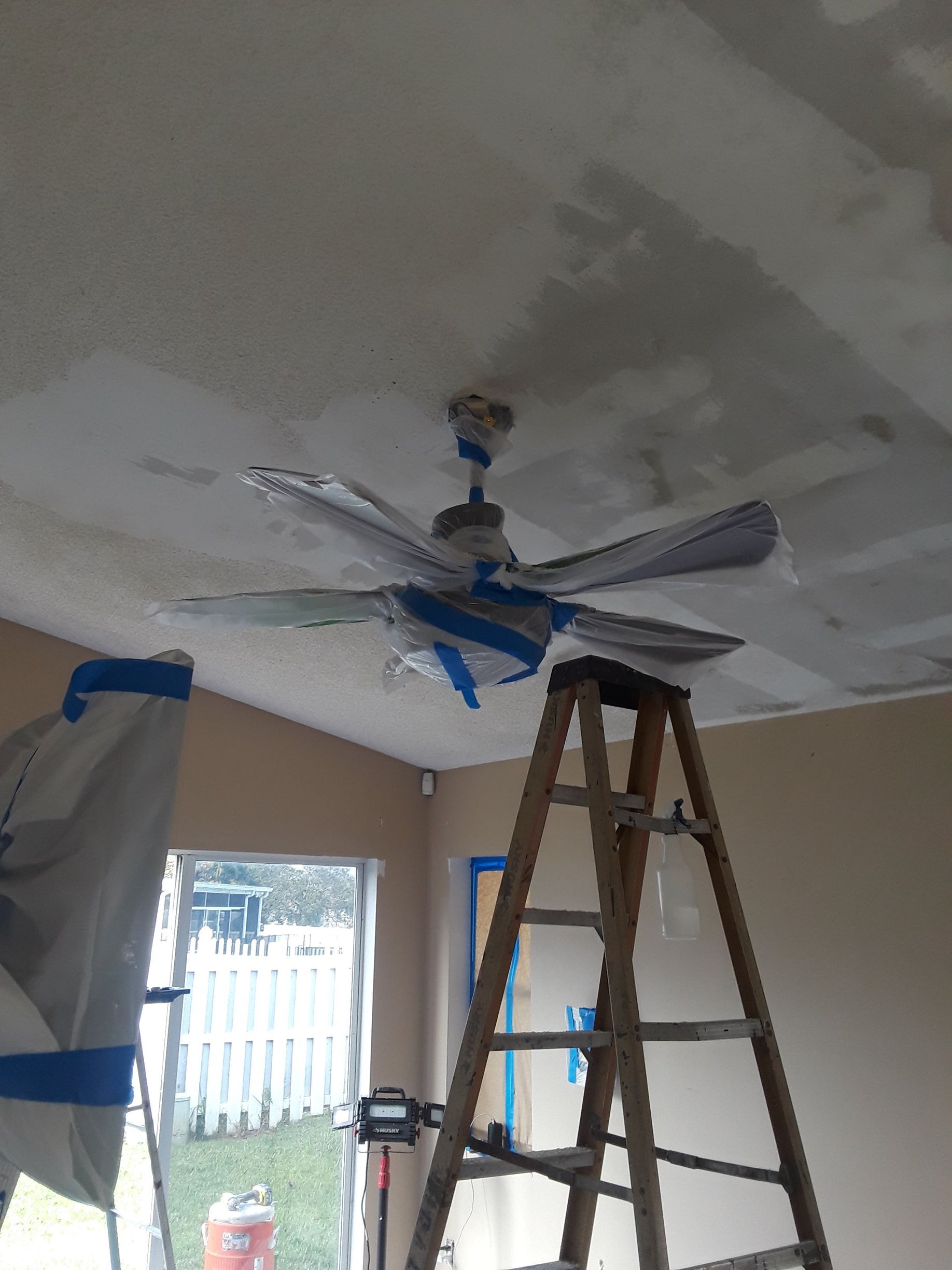 A ceiling fan is being painted in a room with a ladder