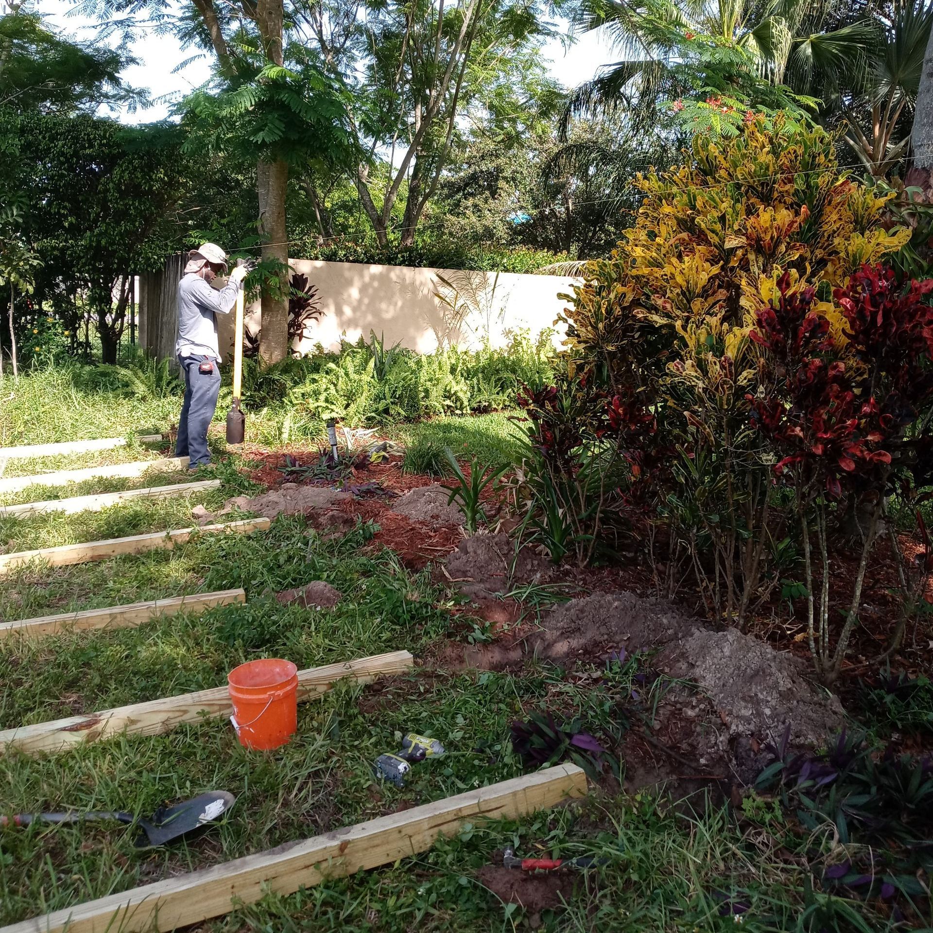A man is standing in the grass in a garden holding a shovel.
