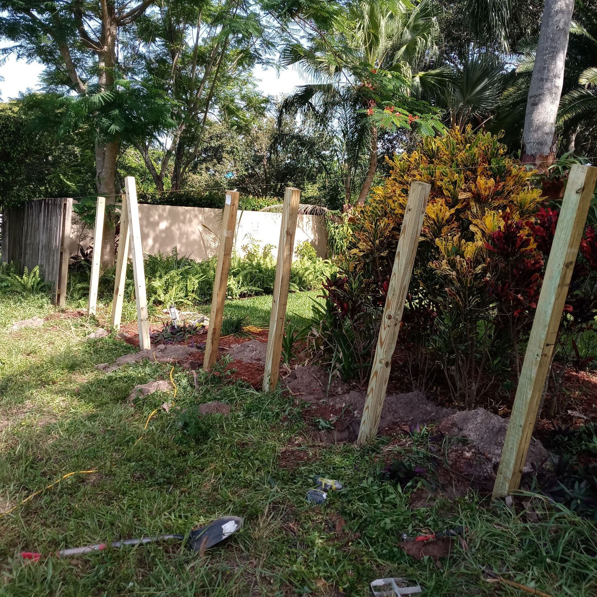 A wooden fence is being built in a yard with trees in the background.