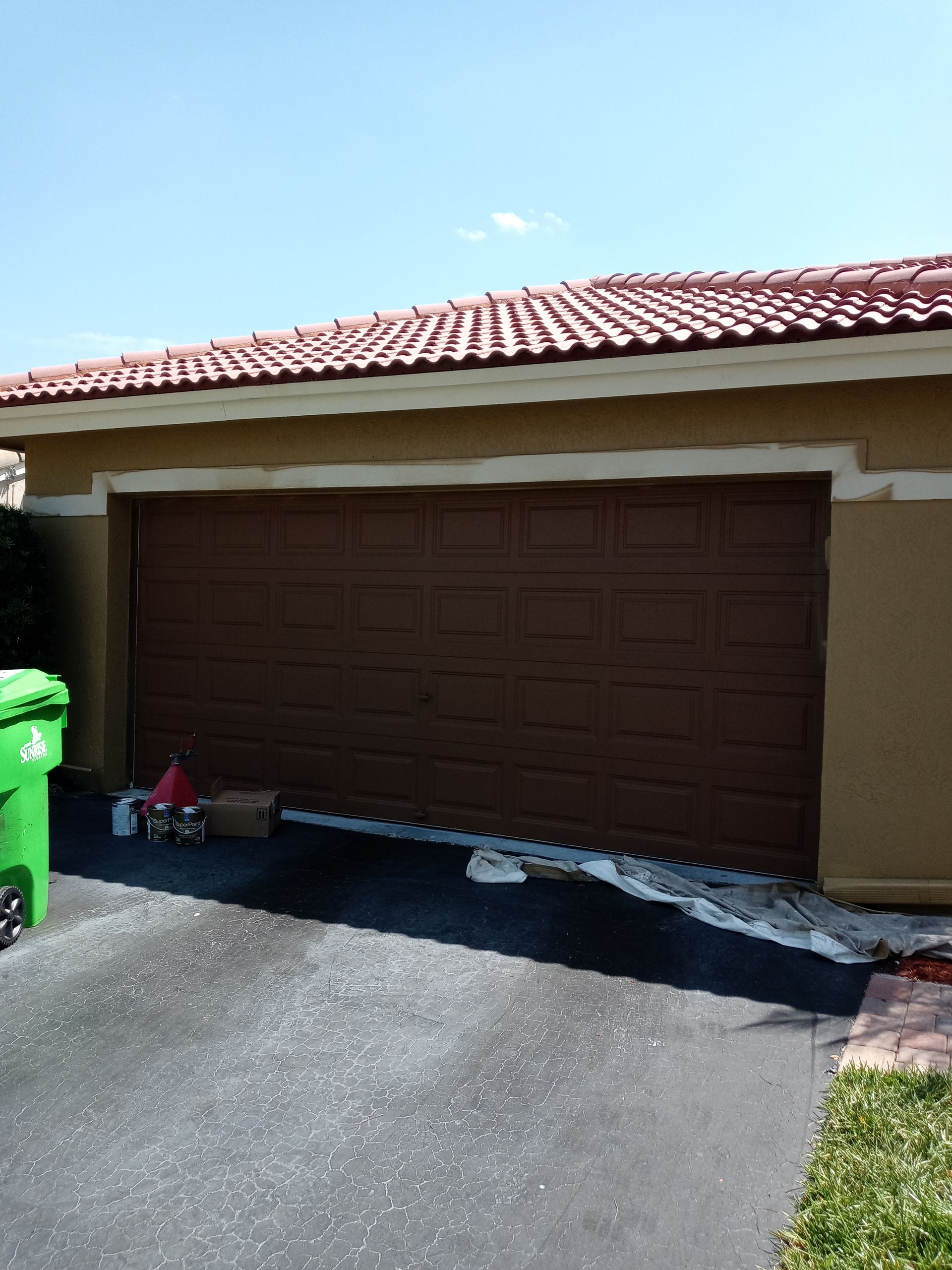A green trash can sits in front of a brown garage door