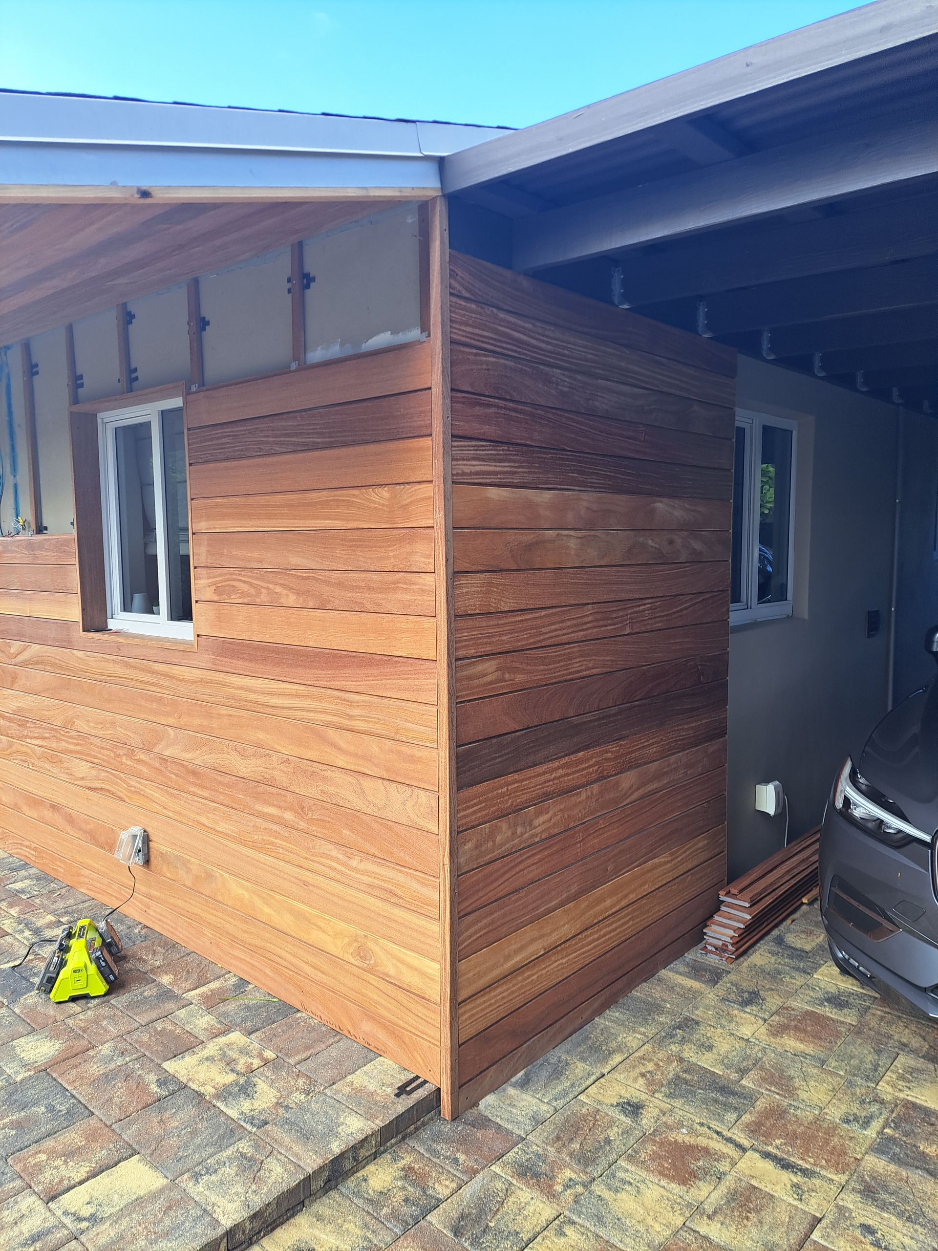 A car is parked in front of a house with wooden siding.