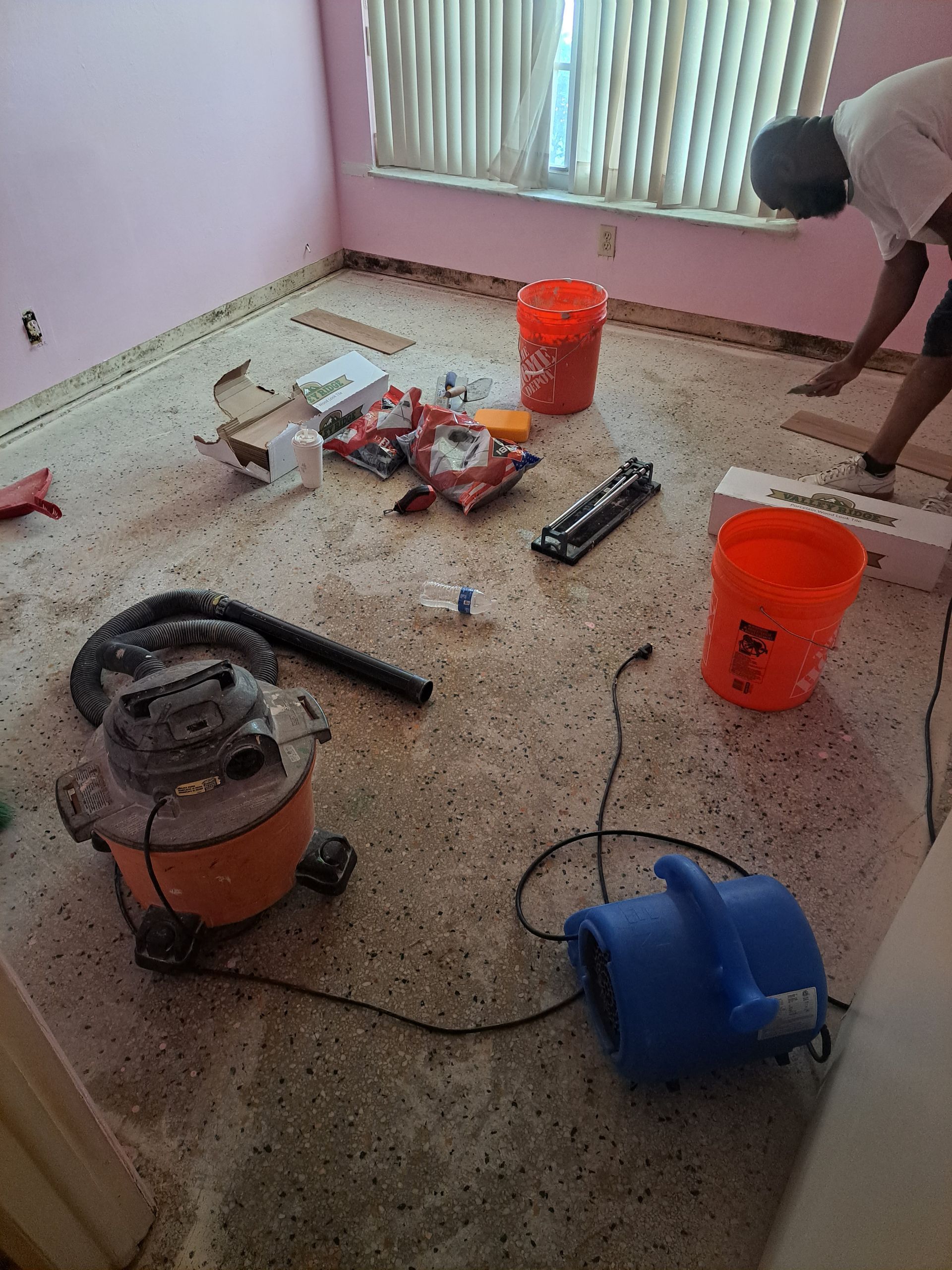 A man is laying carpet in a room with a vacuum cleaner.