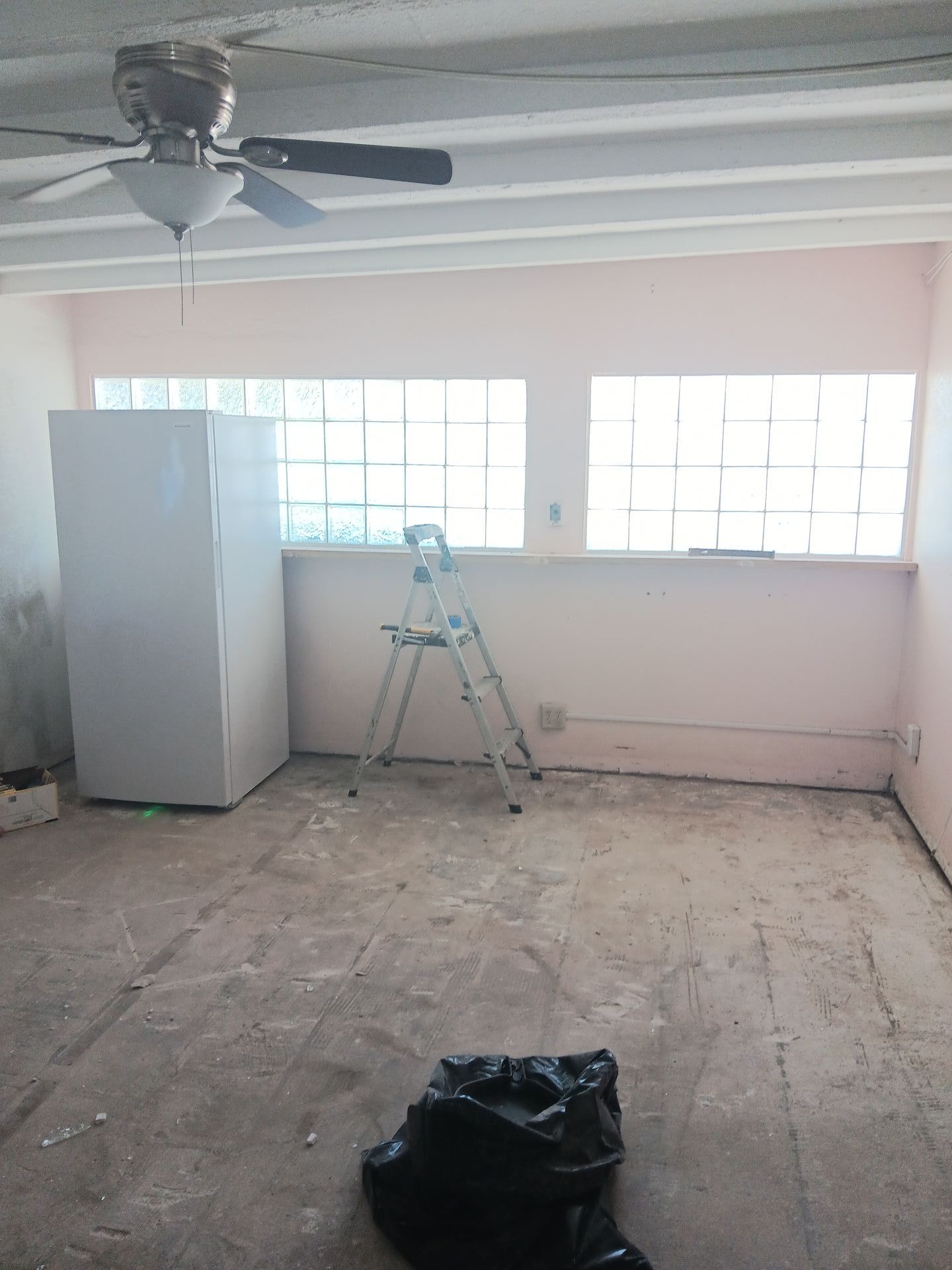 A room with a ceiling fan and a freezer in it.