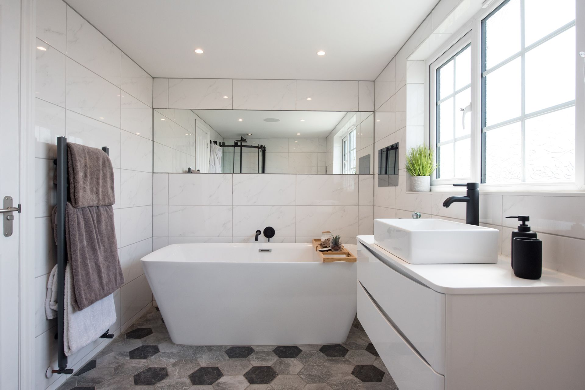 A bathroom with a bathtub , sink , mirror and window.