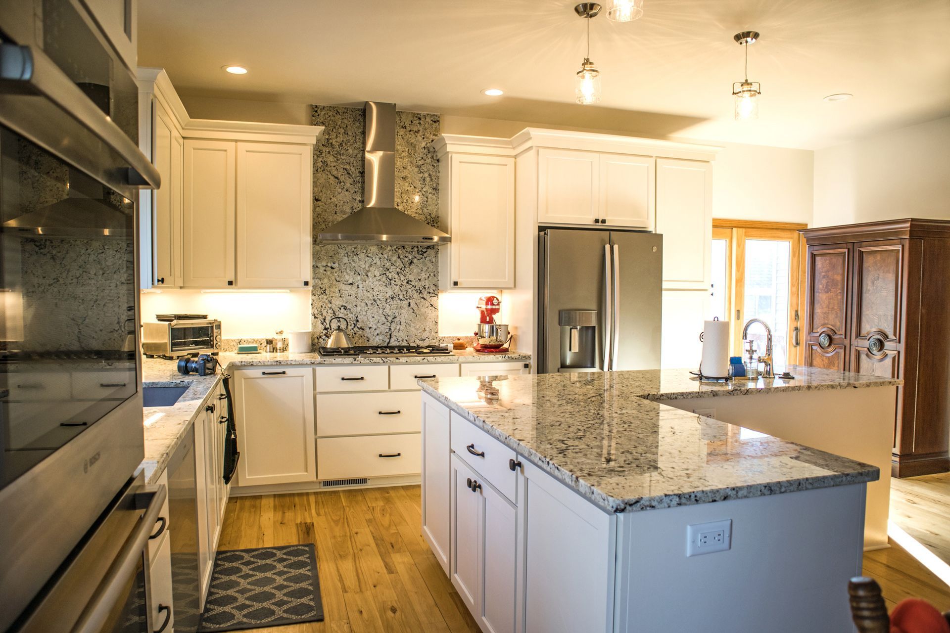 A kitchen with white cabinets , granite counter tops , stainless steel appliances and a large island.