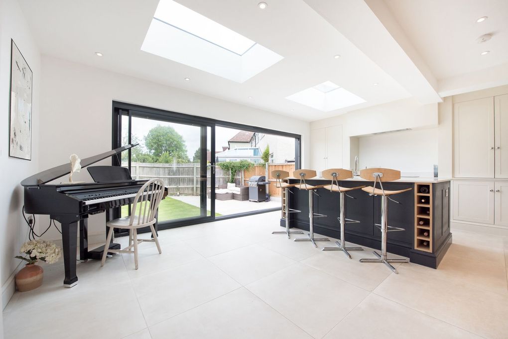 A living room with a piano and a kitchen with sliding glass doors.