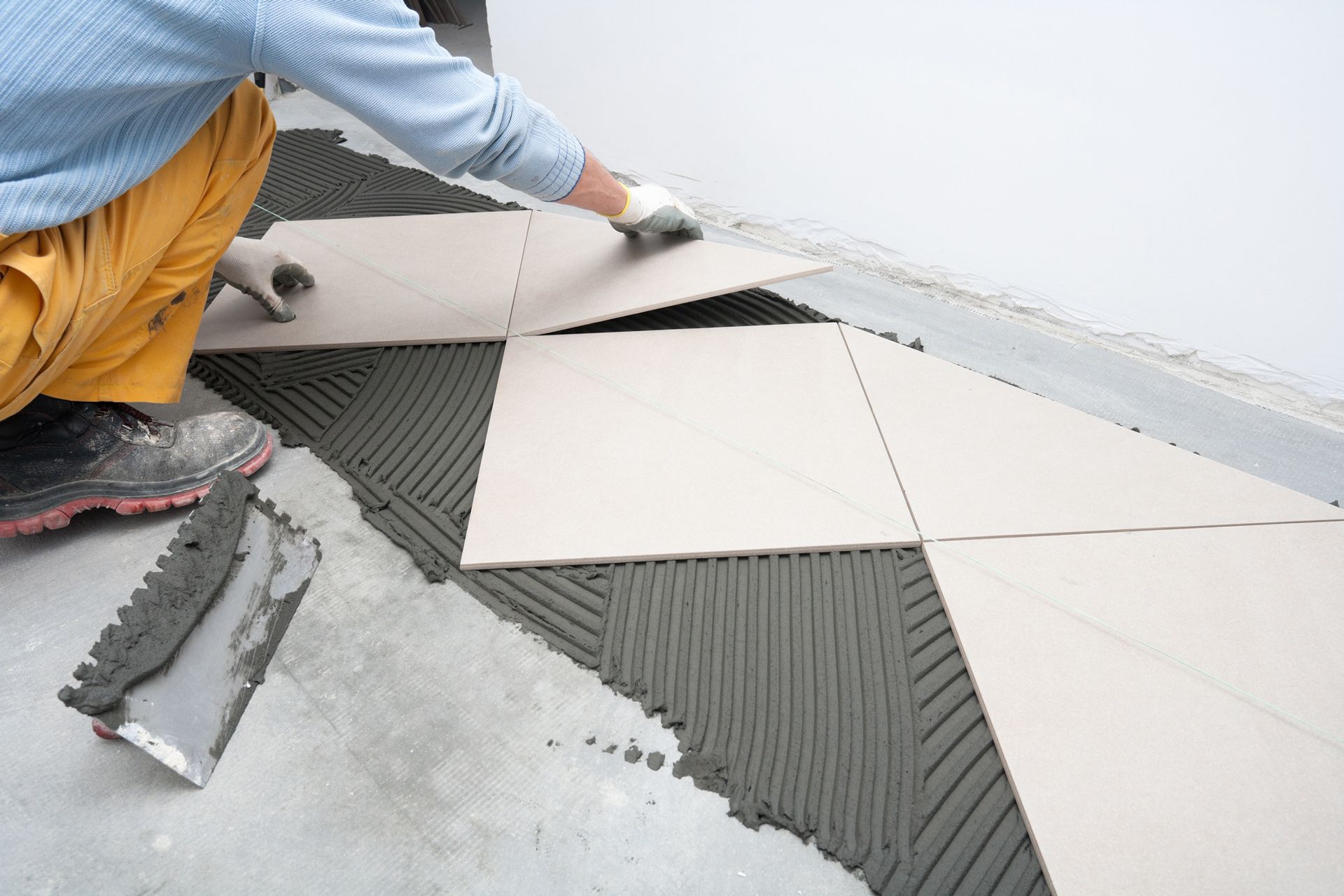 A man is laying tiles on a concrete floor.
