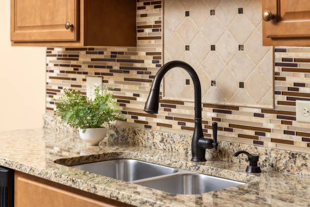 A kitchen sink with a black faucet and a plant on the counter.