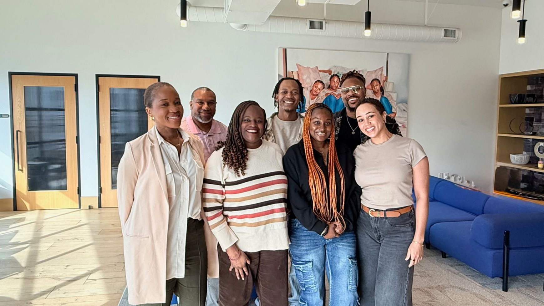 Team photo with 7 people infront of a black stripped wall with the letters E,M,B,E,R