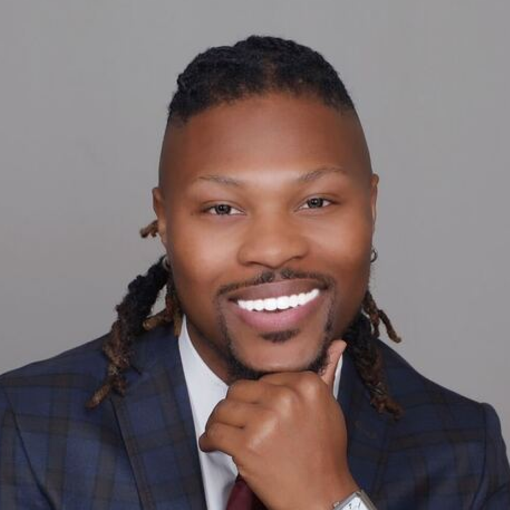 A man in a suit and tie is smiling with his hand on his chin.