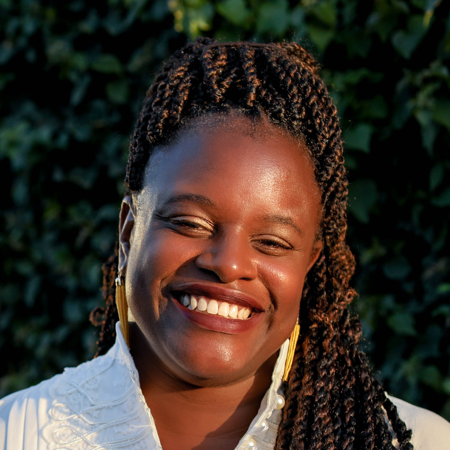 A woman with braids is smiling and wearing a white shirt