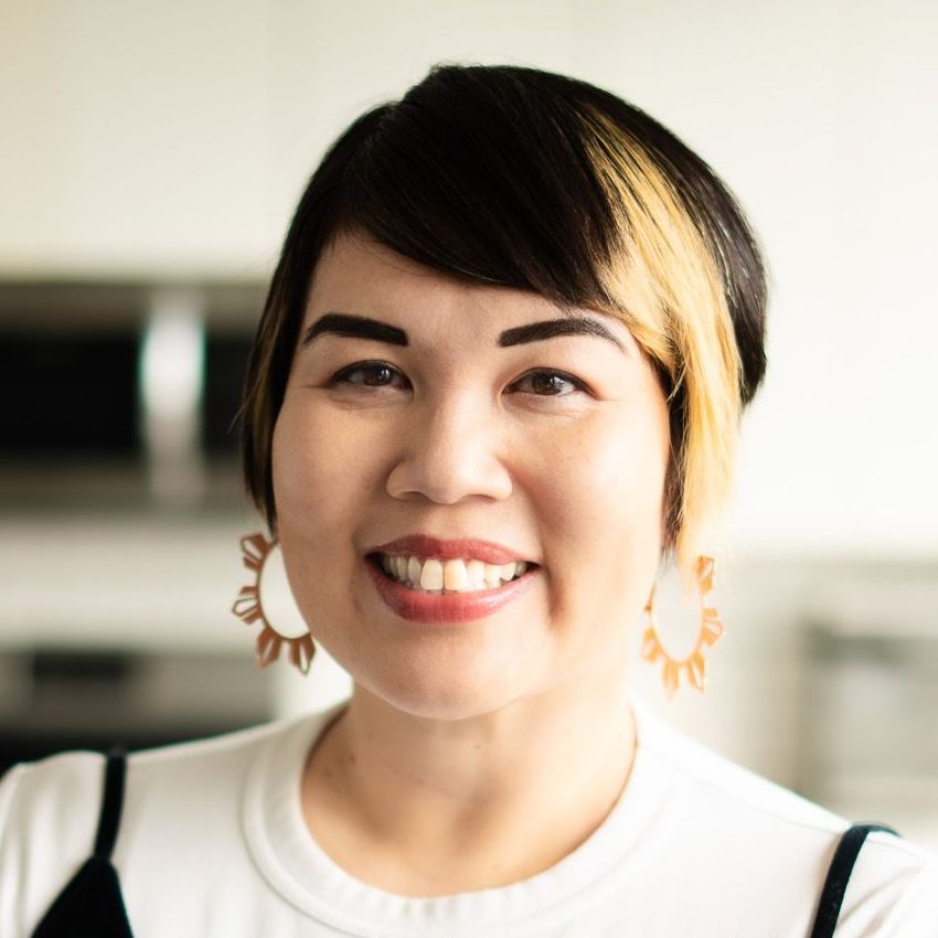 A woman with curly hair is wearing a blue jacket and smiling.
