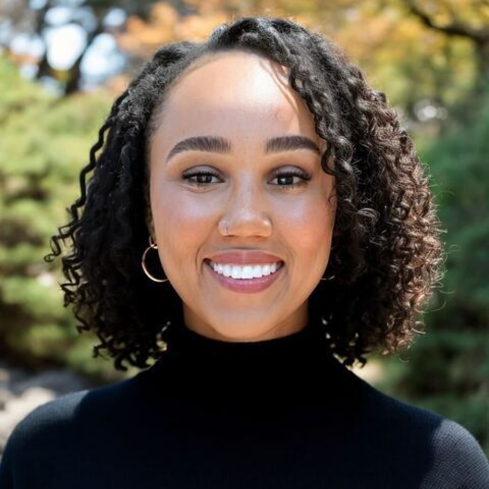 A woman with curly hair is wearing a black turtleneck and smiling