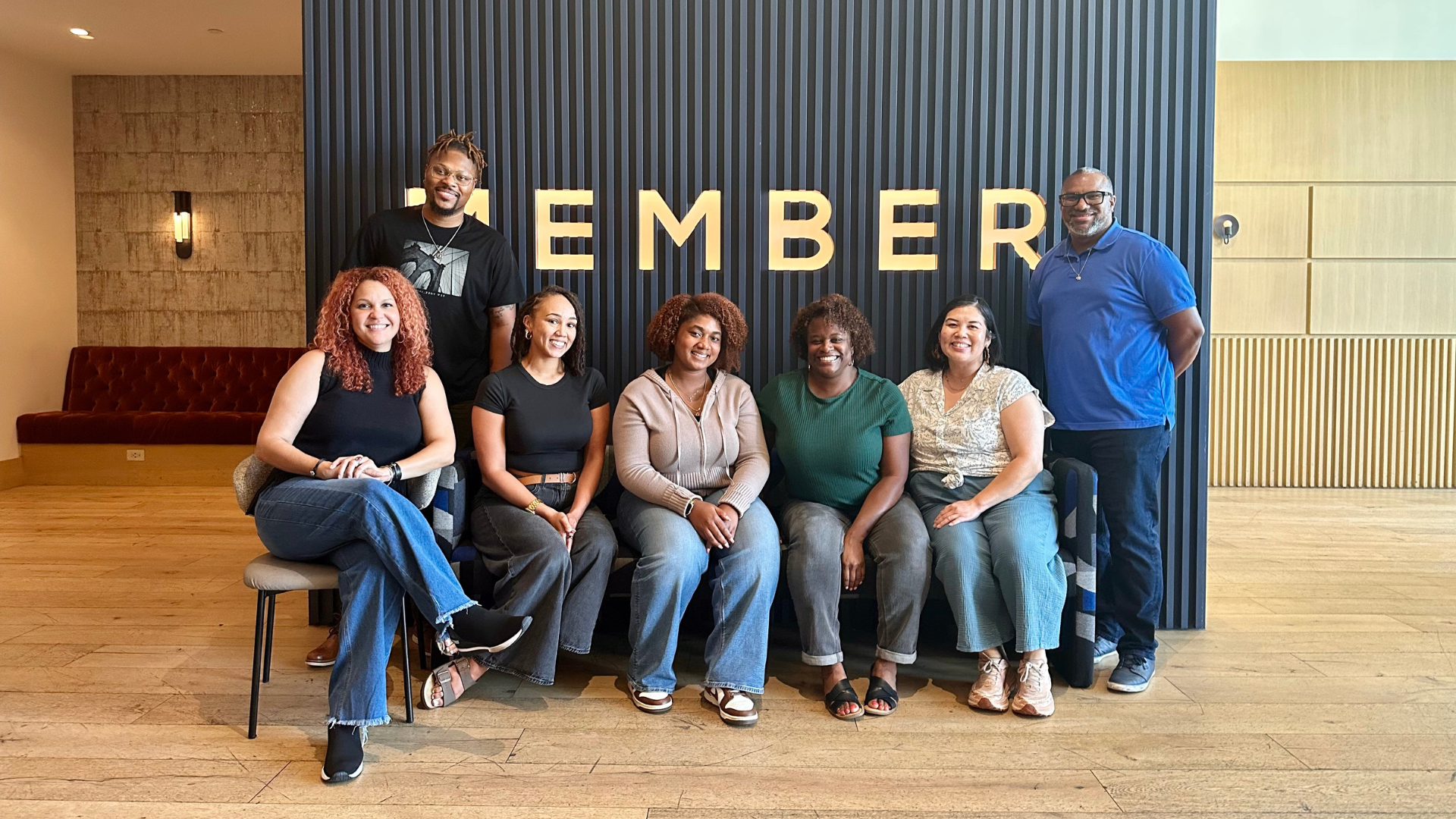 Team photo with 7 people infront of a black stripped wall with the letters E,M,B,E,R