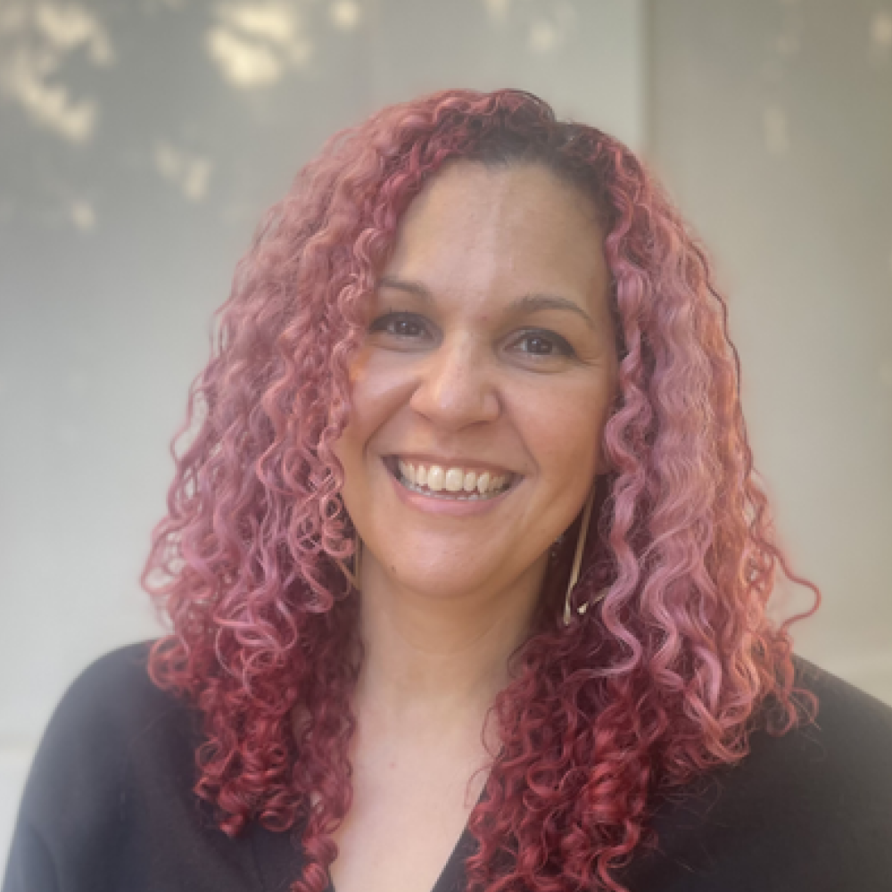 A woman with pink curly hair is smiling for the camera.